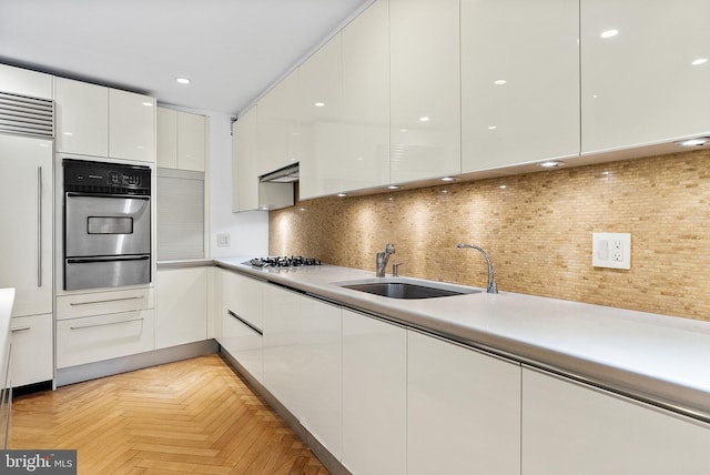 kitchen with sink, light parquet floors, backsplash, stainless steel built in refrigerator, and white cabinetry