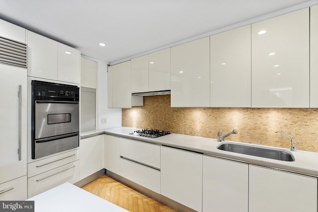 kitchen with backsplash, light parquet flooring, stainless steel appliances, and white cabinetry