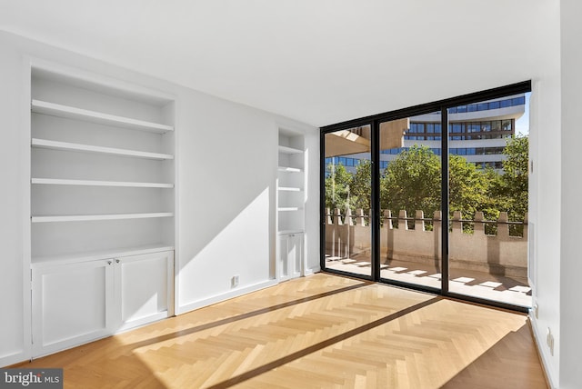 spare room with built in shelves and light parquet flooring