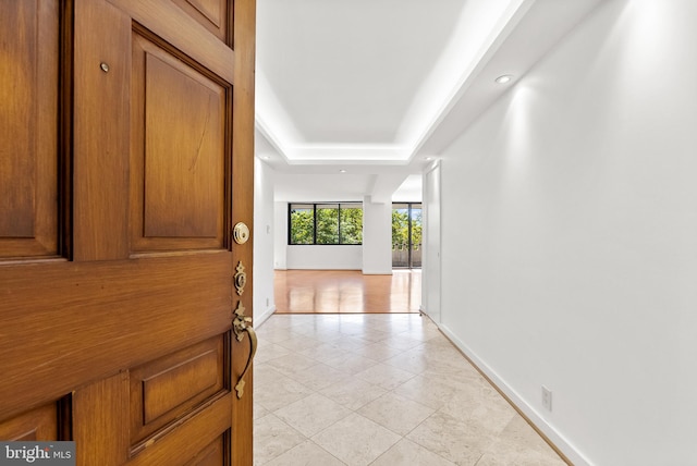 hall with light wood-type flooring and a tray ceiling