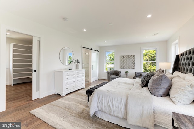 bedroom with a barn door, baseboards, wood finished floors, a spacious closet, and recessed lighting