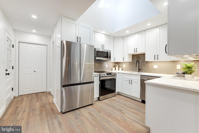 kitchen with stainless steel appliances, light wood-style flooring, light stone countertops, and white cabinets