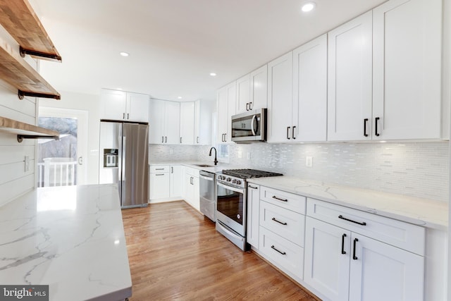 kitchen featuring stainless steel appliances, light stone countertops, white cabinets, and open shelves