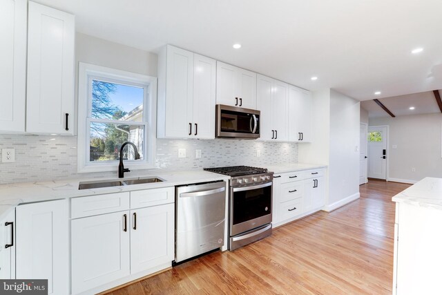 kitchen with stainless steel appliances, light wood-type flooring, white cabinetry, and a sink