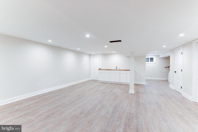 finished basement featuring recessed lighting, a sink, light wood-style flooring, and baseboards