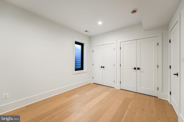 unfurnished bedroom featuring multiple closets, recessed lighting, visible vents, light wood-type flooring, and baseboards