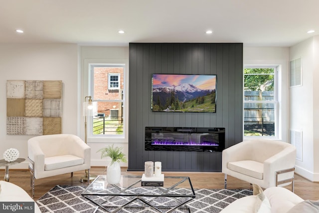 living room with wood finished floors, a glass covered fireplace, visible vents, and recessed lighting