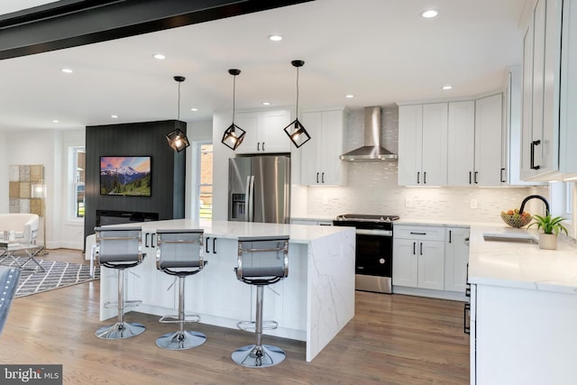 kitchen with white cabinets, a center island, hanging light fixtures, stainless steel appliances, and wall chimney range hood