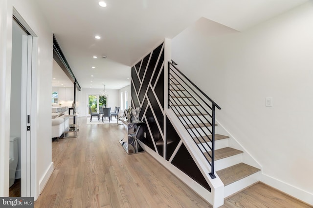 stairs featuring baseboards, an inviting chandelier, wood finished floors, and recessed lighting