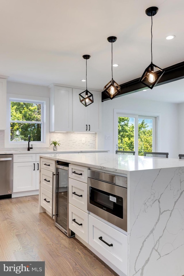 kitchen with tasteful backsplash, hanging light fixtures, stainless steel dishwasher, white cabinetry, and beverage cooler