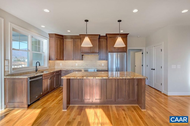 kitchen with light hardwood / wood-style floors, stainless steel appliances, pendant lighting, and light stone counters