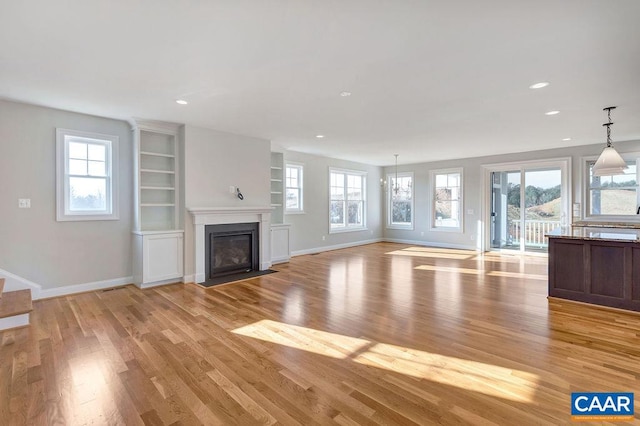 unfurnished living room featuring an inviting chandelier and light wood-type flooring