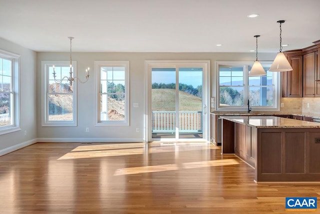 kitchen with a notable chandelier, hanging light fixtures, light stone counters, and light hardwood / wood-style floors