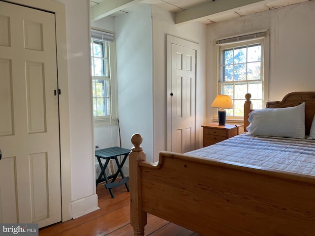 bedroom featuring beamed ceiling, multiple windows, and light wood-type flooring