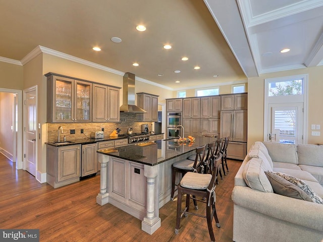 kitchen with a breakfast bar, wall chimney range hood, dark hardwood / wood-style flooring, ornamental molding, and a kitchen island with sink