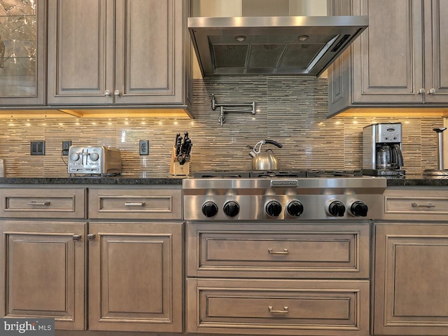 kitchen with wall chimney range hood, tasteful backsplash, stainless steel gas stovetop, and dark stone counters