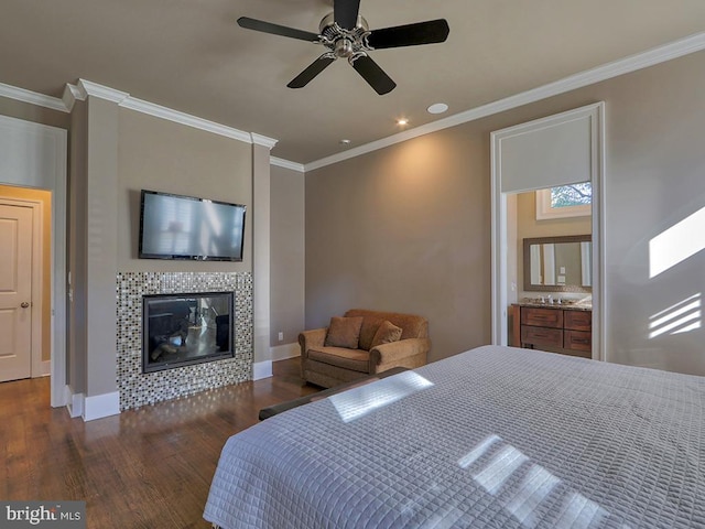 bedroom featuring crown molding, connected bathroom, dark wood-type flooring, a tile fireplace, and ceiling fan