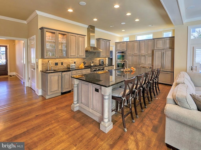 kitchen featuring sink, wall chimney range hood, dark wood-type flooring, a kitchen breakfast bar, and a kitchen island with sink