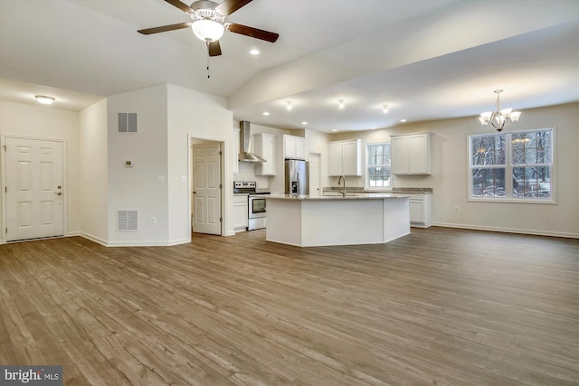 kitchen featuring white cabinets, light hardwood / wood-style flooring, stainless steel appliances, wall chimney range hood, and decorative light fixtures