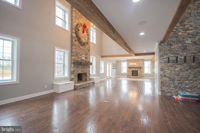 unfurnished living room featuring beamed ceiling, hardwood / wood-style floors, a stone fireplace, and plenty of natural light