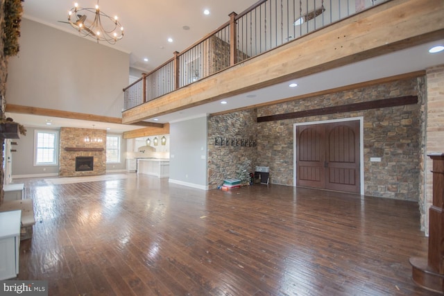 unfurnished living room featuring hardwood / wood-style flooring, beamed ceiling, a fireplace, a high ceiling, and a chandelier