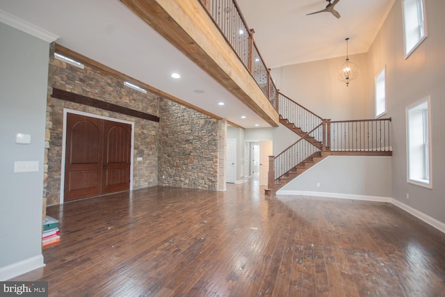 unfurnished living room featuring a towering ceiling, ceiling fan with notable chandelier, crown molding, beam ceiling, and dark hardwood / wood-style floors