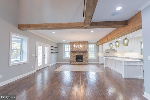 unfurnished living room with beamed ceiling, a healthy amount of sunlight, dark wood-type flooring, and french doors