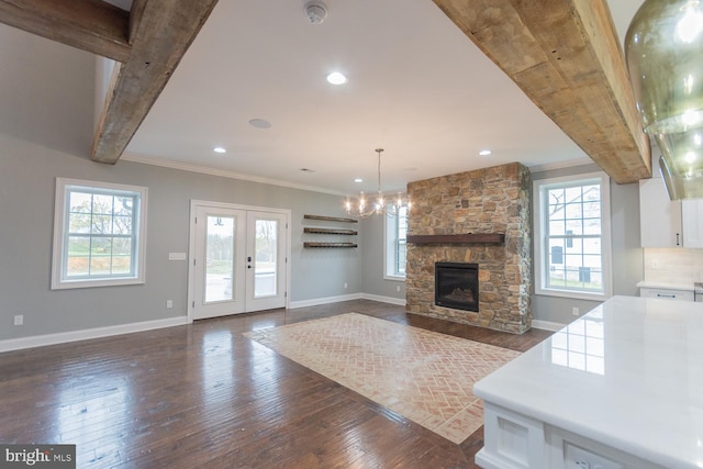 unfurnished living room featuring french doors, ornamental molding, dark wood-type flooring, beamed ceiling, and a stone fireplace