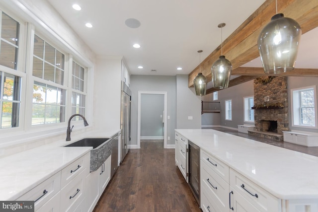 kitchen with a stone fireplace, sink, dark hardwood / wood-style floors, beamed ceiling, and decorative light fixtures