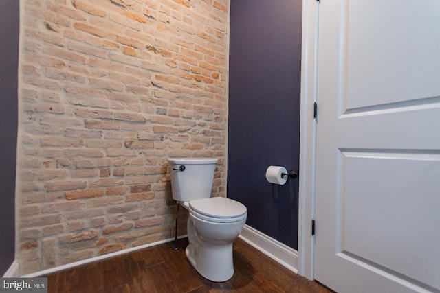 bathroom featuring hardwood / wood-style flooring, toilet, and brick wall