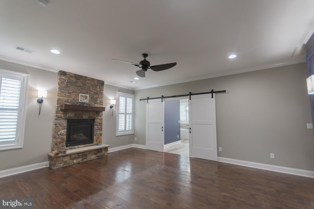 unfurnished living room with a barn door, dark hardwood / wood-style flooring, a healthy amount of sunlight, and ornamental molding
