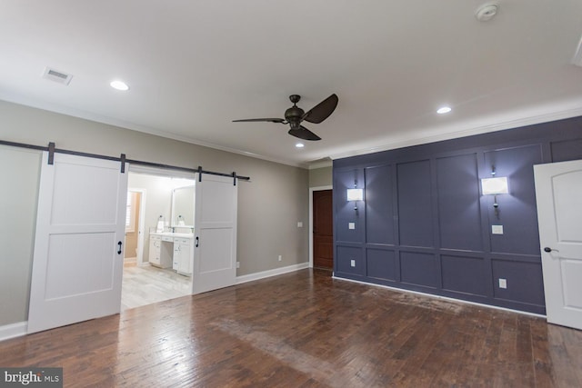unfurnished bedroom featuring ensuite bath, ceiling fan, crown molding, a barn door, and hardwood / wood-style floors