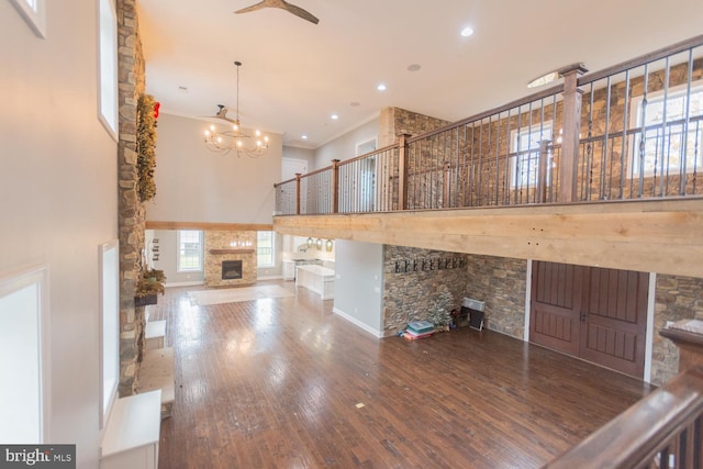 unfurnished living room with hardwood / wood-style floors, ceiling fan with notable chandelier, a stone fireplace, and a towering ceiling