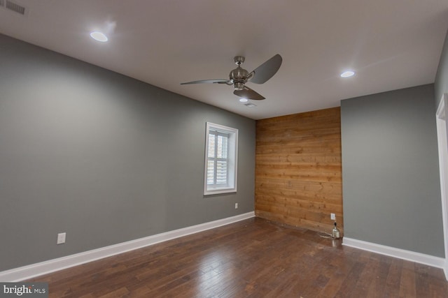 spare room with ceiling fan, wood walls, and dark wood-type flooring