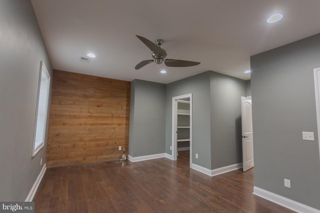 empty room with ceiling fan, dark hardwood / wood-style flooring, and wooden walls