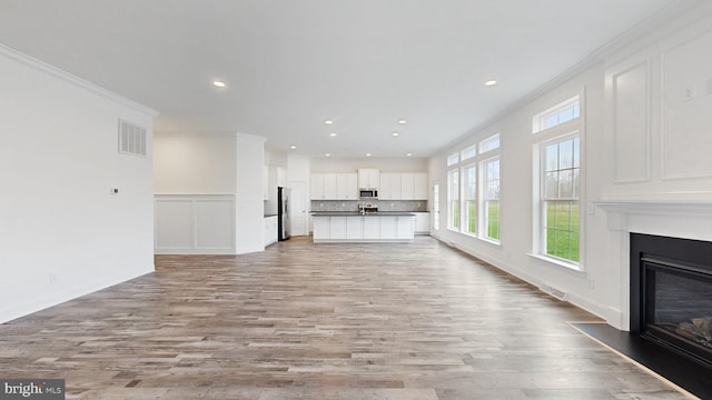 unfurnished living room with light hardwood / wood-style floors and crown molding