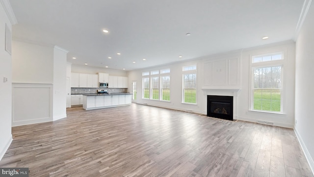 unfurnished living room featuring ornamental molding, light hardwood / wood-style floors, and a healthy amount of sunlight