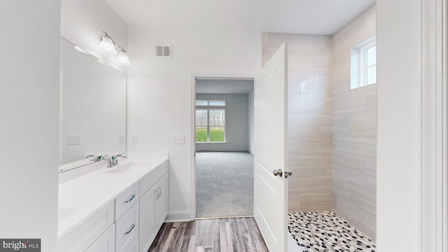 bathroom with hardwood / wood-style flooring, vanity, and a tile shower