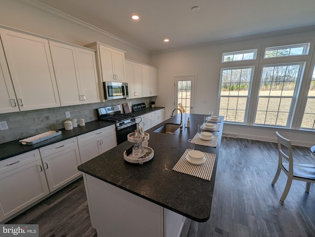 kitchen with tasteful backsplash, stainless steel appliances, sink, a center island with sink, and white cabinetry