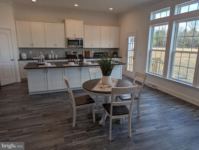 kitchen with appliances with stainless steel finishes, backsplash, a center island with sink, dark hardwood / wood-style floors, and white cabinetry