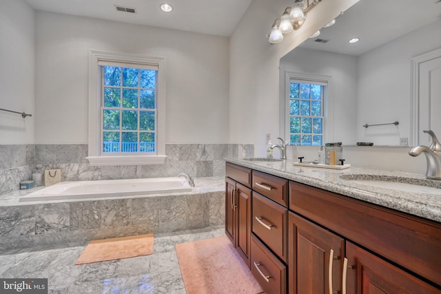 bathroom with tiled bath, plenty of natural light, double sink, and vanity with extensive cabinet space