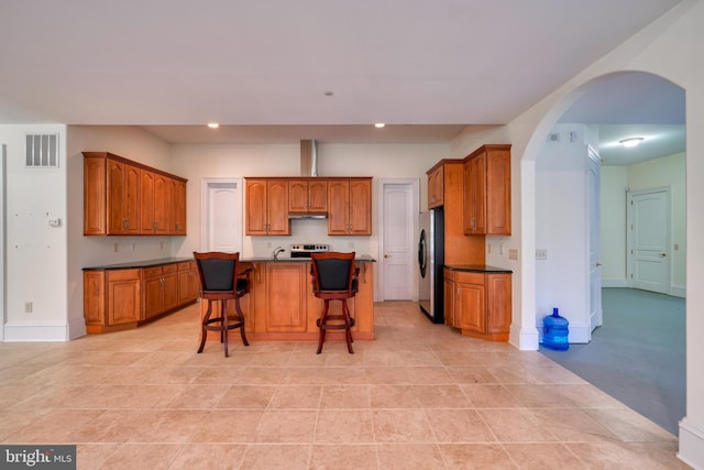 kitchen featuring stainless steel refrigerator, a breakfast bar area, a kitchen island with sink, and light tile flooring