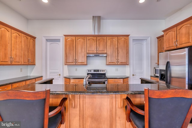 kitchen featuring appliances with stainless steel finishes, dark stone countertops, and a breakfast bar area