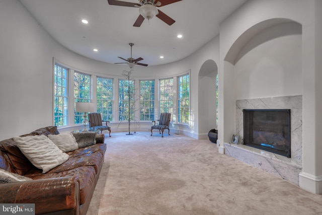 living room featuring ceiling fan, light colored carpet, and a high end fireplace