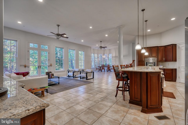 kitchen with decorative light fixtures, light stone countertops, ceiling fan, stainless steel oven, and a center island with sink