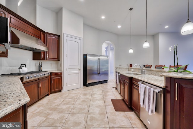 kitchen with pendant lighting, sink, light stone counters, stainless steel appliances, and wall chimney range hood