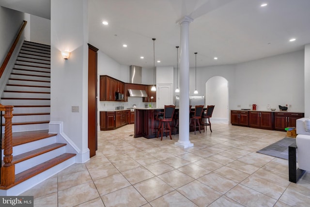 kitchen featuring a kitchen island, a breakfast bar, light tile floors, decorative light fixtures, and ornate columns