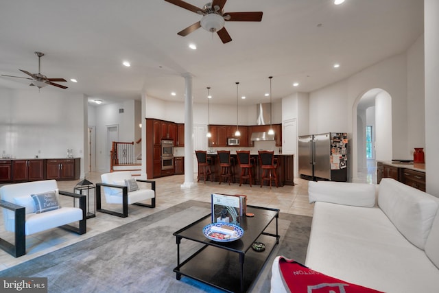 tiled living room with a towering ceiling, ceiling fan, and decorative columns