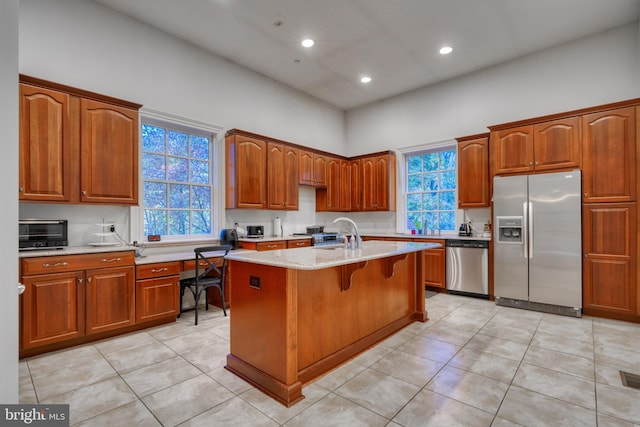 kitchen featuring light tile floors, an island with sink, light stone counters, and stainless steel appliances