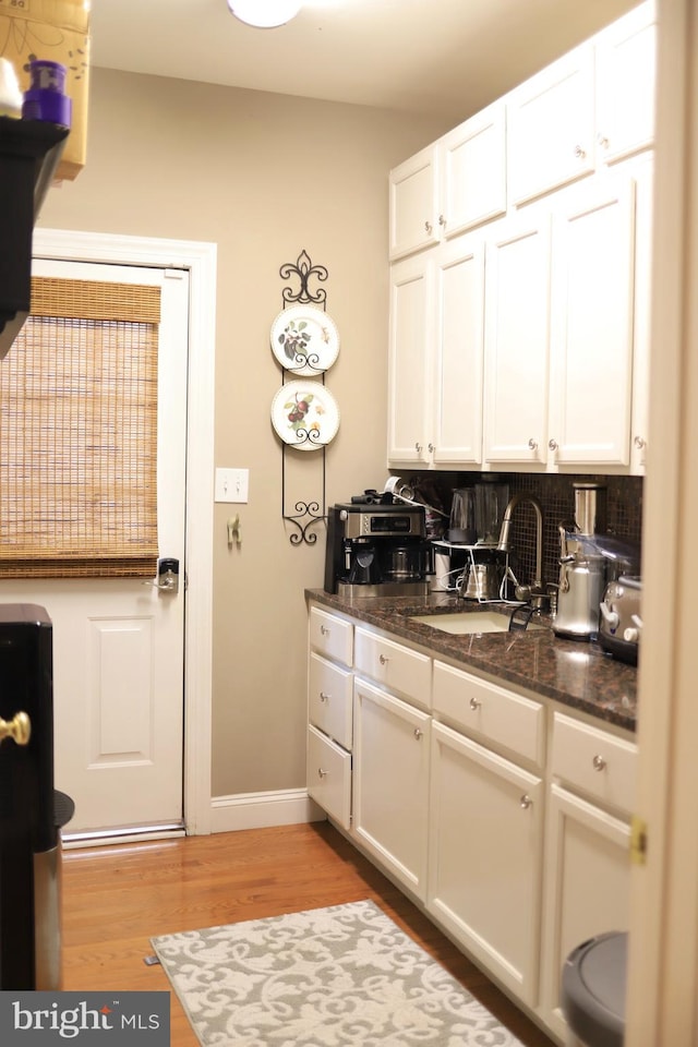 kitchen with backsplash, dark stone counters, sink, white cabinets, and light hardwood / wood-style floors